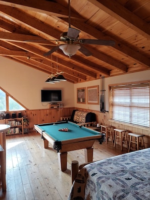 Interior de madeira com mesa de bilhar, televisão e ventoinha no teto.
