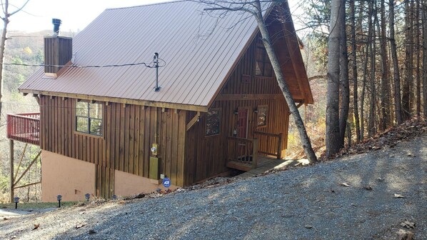 A cabin with a metal roof, wooden walls, a porch, and a gravel driveway.