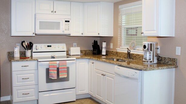A kitchen with white cabinets, a microwave, a stove, a dishwasher, and a coffee maker.