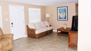 A living room with a beige sofa, a brown armchair, a coffee table, and a television on a stand.
