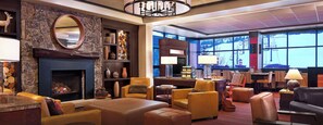 A spacious lounge with leather sofas, a fireplace, and a large window offering a view of a snowy landscape.
