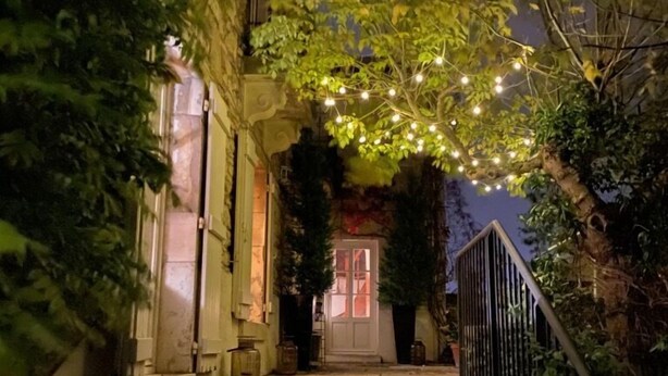 A staircase leading to a building with a door, surrounded by greenery and string lights.