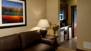 A living room with a brown leather sofa, a table with a lamp, a framed painting, and a vase with flowers.