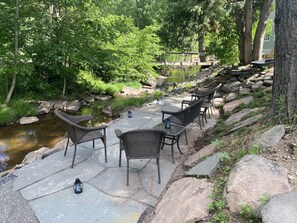 An outdoor patio with stone flooring, wicker furniture, and lanterns. - Charming Mountain Retreat Lg Mod/Kit on Stream/Fire-pit/Hot Tub (Windham)