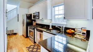 A modern kitchen with white cabinets, a black refrigerator, stainless steel appliances, a granite countertop, and a window providing natural light.