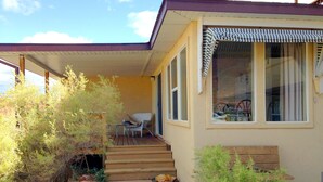 A single-story house with a covered porch, a small outdoor seating area, and a window with a striped awning. - Beautiful Views Overlooking Moab Valley! (Moab)