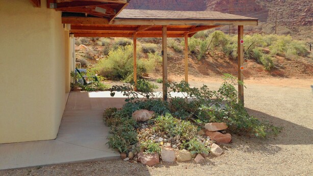 A covered outdoor area with a wooden pergola, a concrete pathway, and a garden with rocks and desert plants. - Beautiful Views Overlooking Moab Valley! (Moab)