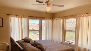 A bedroom with a bed, a chair, a ceiling fan, and large windows with curtains. - Beautiful Views Overlooking Moab Valley! (Moab)