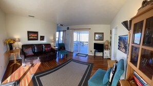 A spacious living room with a leather sofa, a teal armchair, and a wooden coffee table. There is a large rug on the floor, a television on a stand, and a bookshelf filled with books. - Beautiful Views Overlooking Moab Valley! (Moab)
