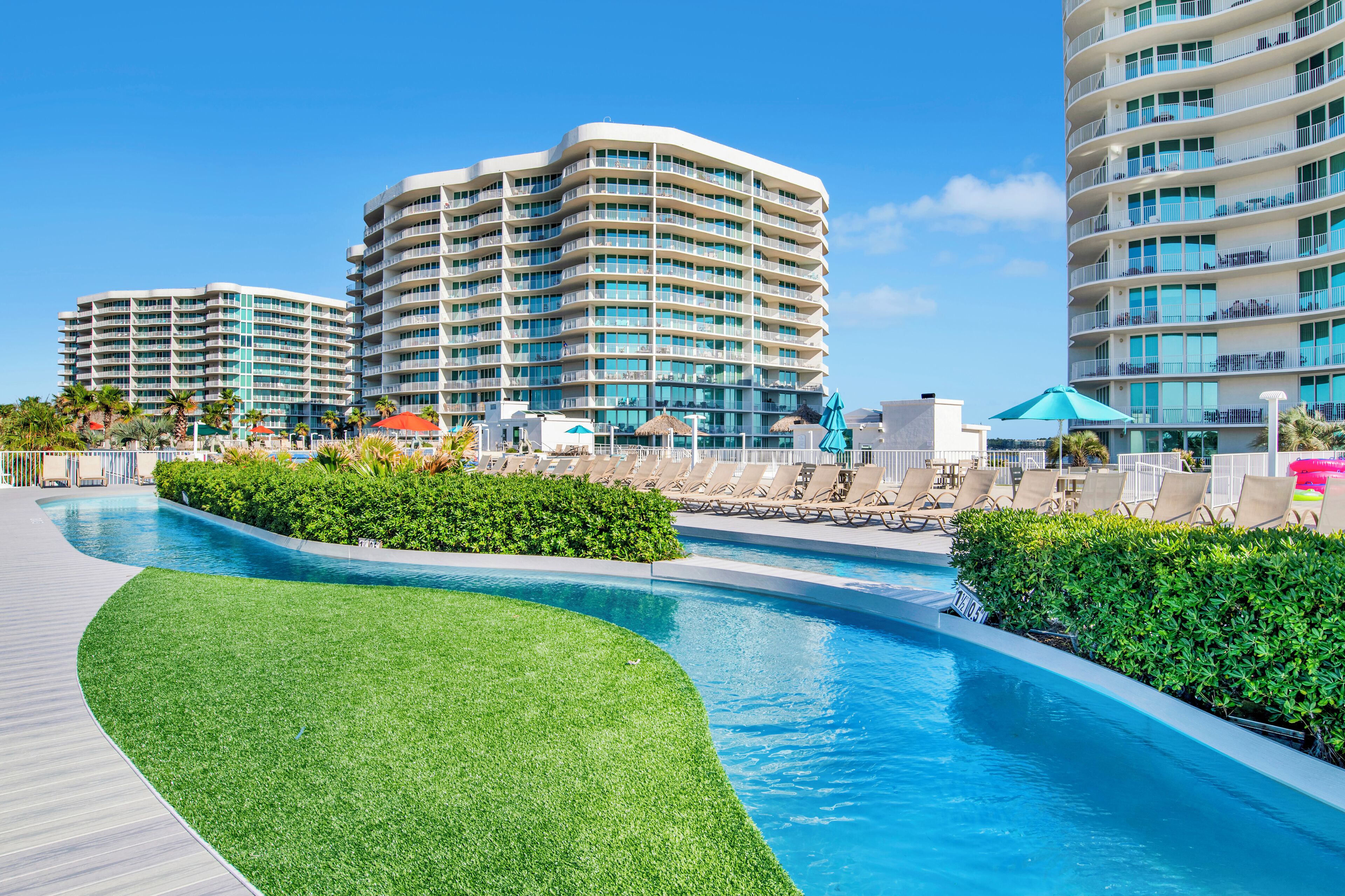 A modern hotel with a pool area, multiple balconies, and lush greenery.