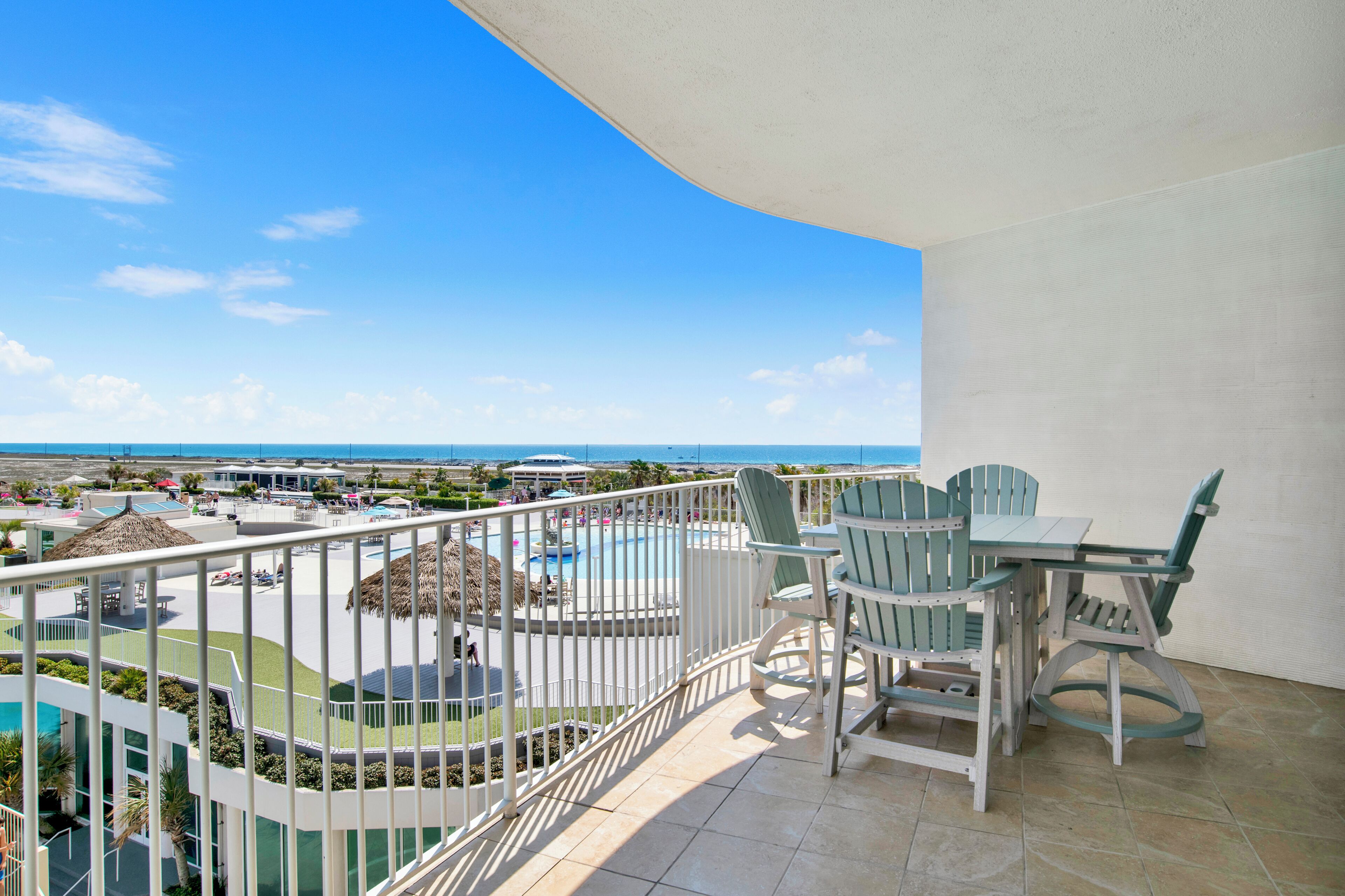 Un balcon donnant sur une piscine et une zone de loisirs, une table avec des chaises et une rambarde.