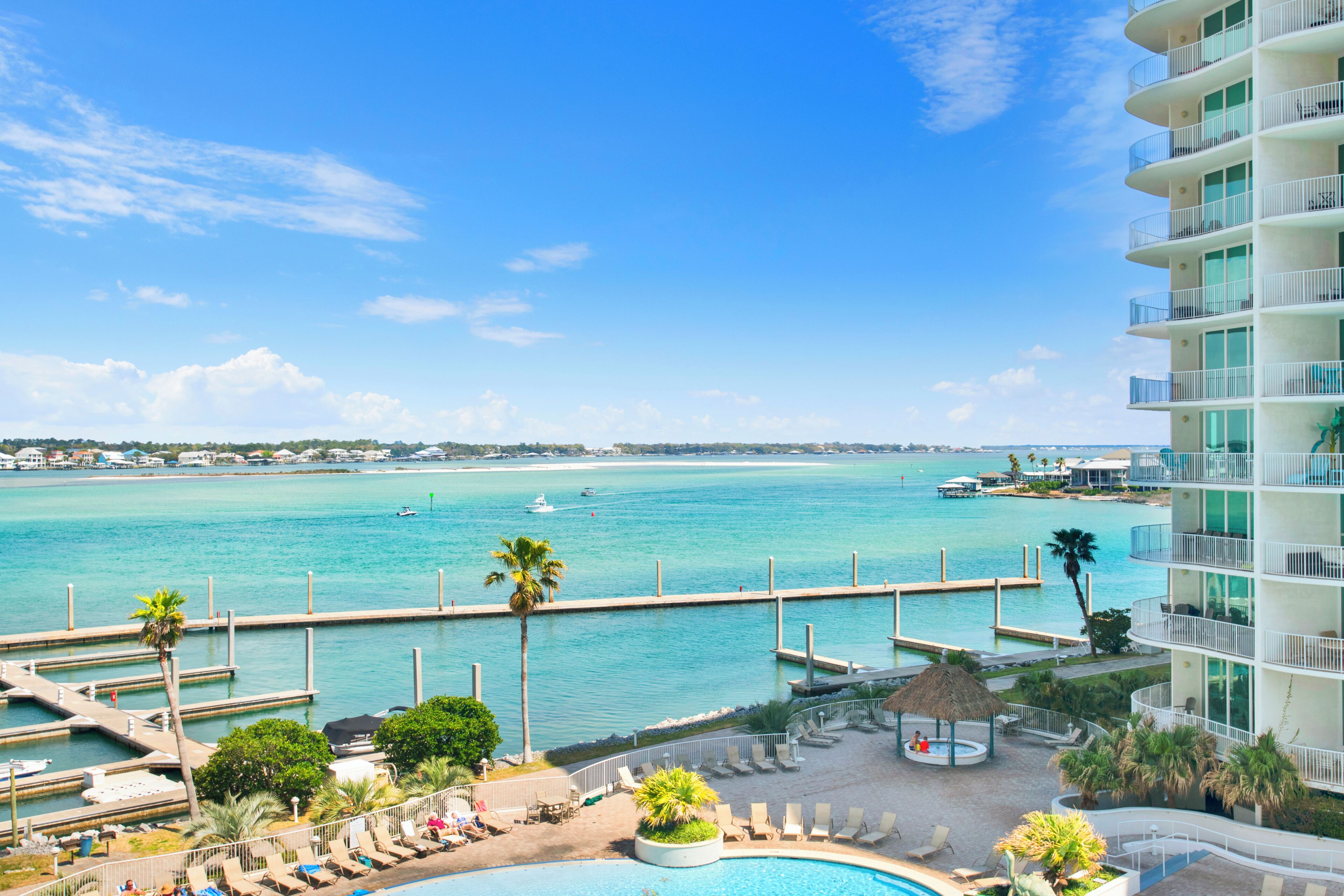 A resort with a swimming pool, lounge chairs, a dock, and a view of the sea.