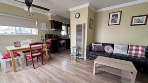 A living room with a dining area, a black leather sofa, a wooden coffee table, a kitchen with a microwave, and a ceiling fan.