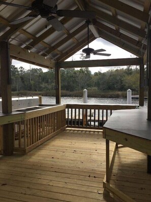 A covered wooden deck with a view of a water body and trees.