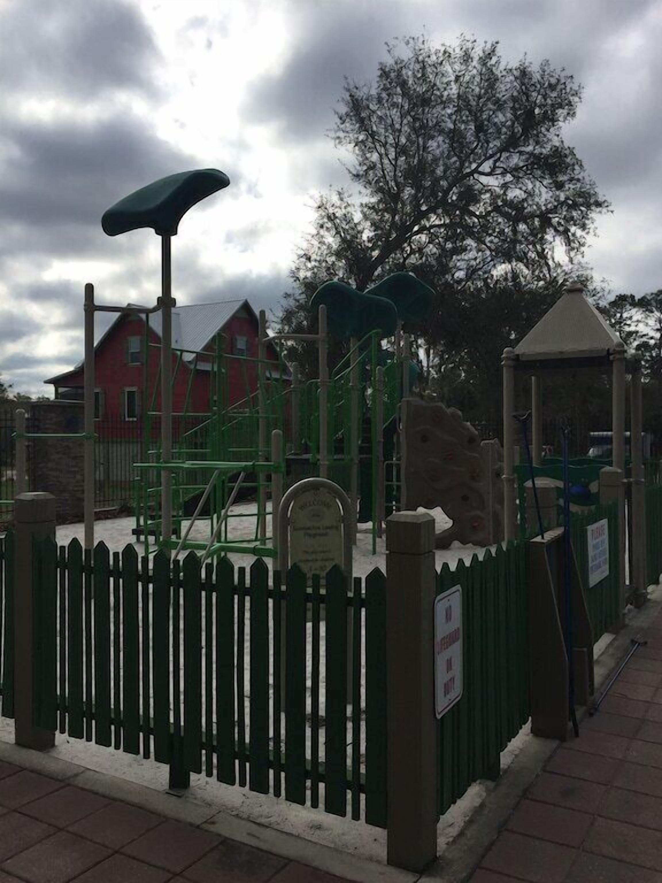 Un parque infantil con estructuras para escalar y un pabellón, rodeado por una cerca verde.