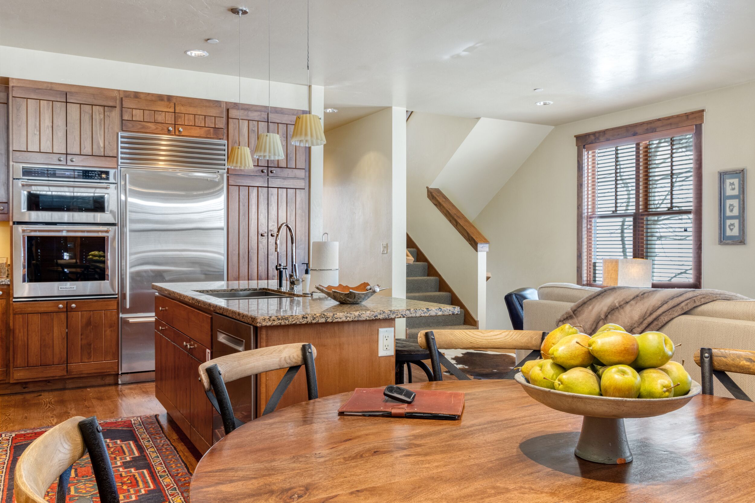 A modern kitchen with wooden cabinets, stainless steel appliances, and a dining area with a table set for two.