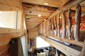 A cabin interior with a loft bed, wooden walls, a small kitchenette, and a window. - Unique Treehouse near Zion with King Bed (Orderville)
