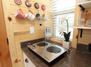 A kitchen with wooden walls, a black countertop, and a stainless steel cuimax cooktop. - Unique Treehouse near Zion with King Bed (Orderville)
