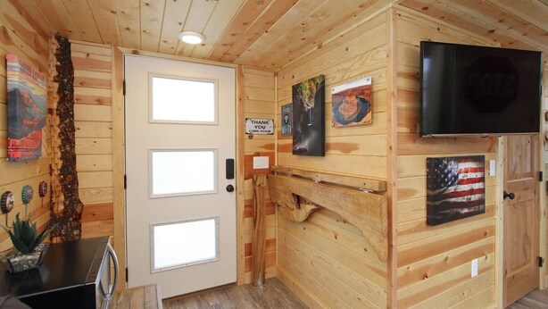 Un interior de madera con un televisor montado en la pared, una puerta con ventanal y obras de arte en las paredes.