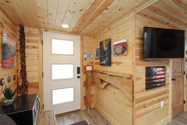 A wooden interior with a television mounted on the wall, a door with a window, and artwork on the walls.