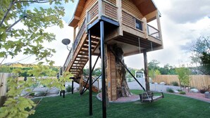 Una casa en el árbol con fachada de madera, una escalera y un columpio.