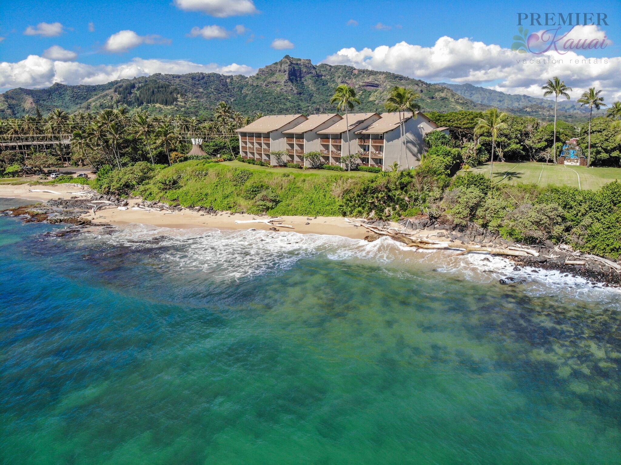 A beachfront hotel with multiple buildings, a sandy beach, and a mountain in the background.
