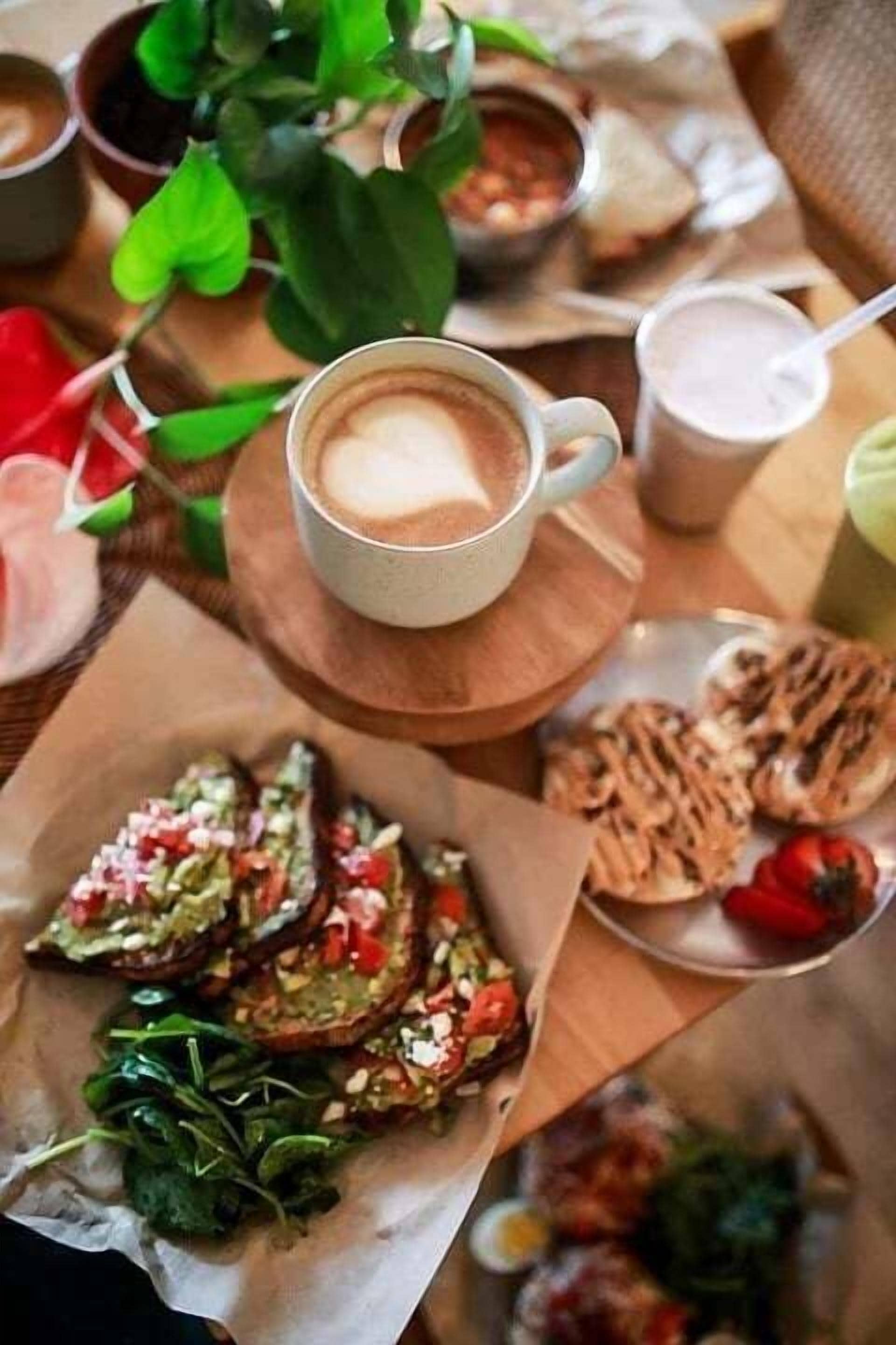 A table with a cup of coffee, a plate of food, and a bowl of soup.