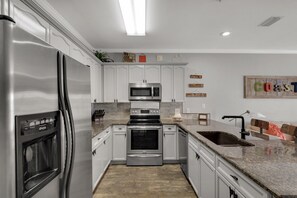 Una cocina moderna con armarios blancos, electrodomésticos de acero inoxidable, encimeras de granito y horno empotrado.