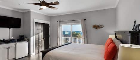 Ein Schlafzimmer mit Bett, Nachttisch, Lampe, Deckenventilator, Fernseher und einem Balkon mit Blick.