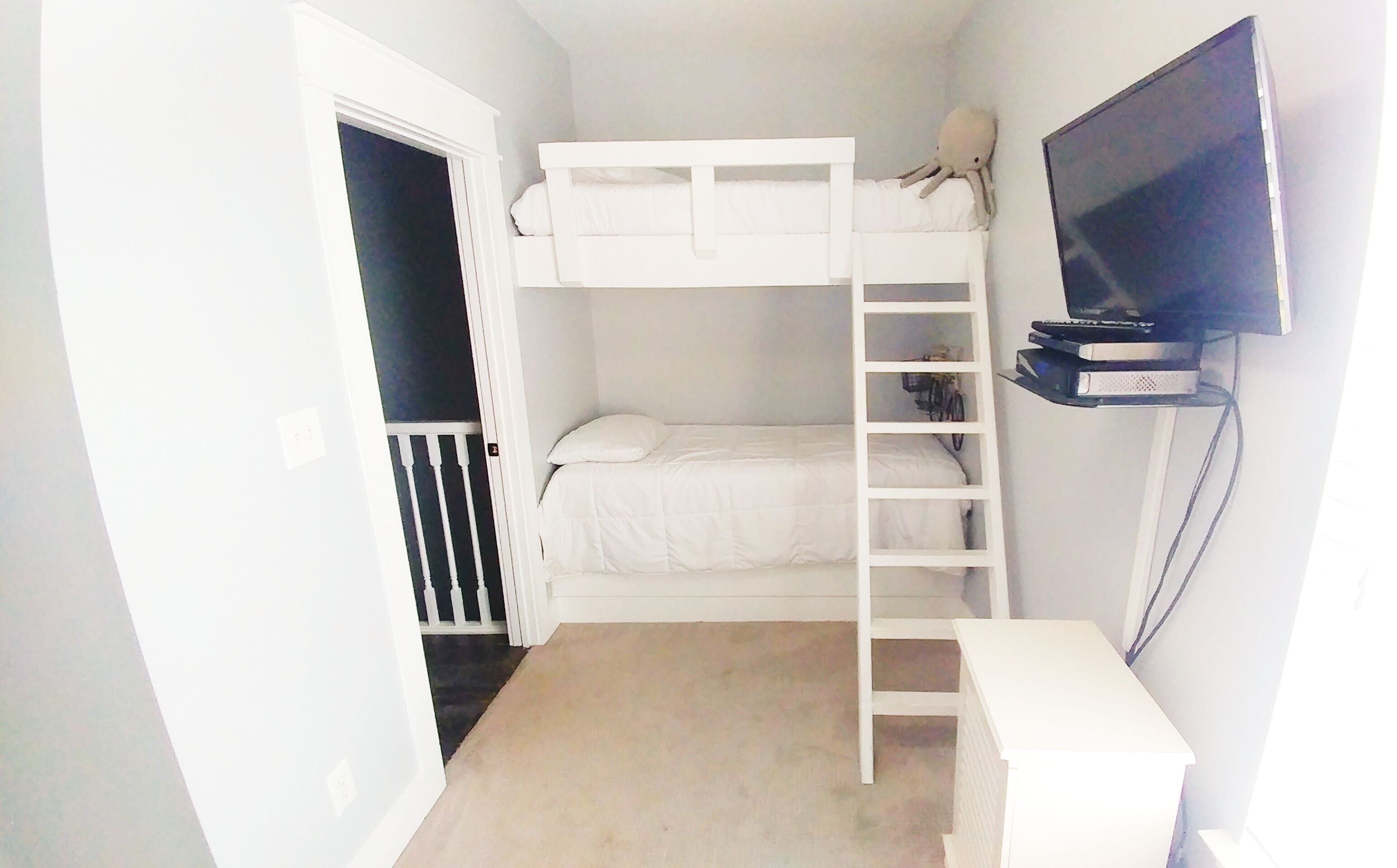 A bunk bed room with a TV on a stand, a ladder, and a closet.