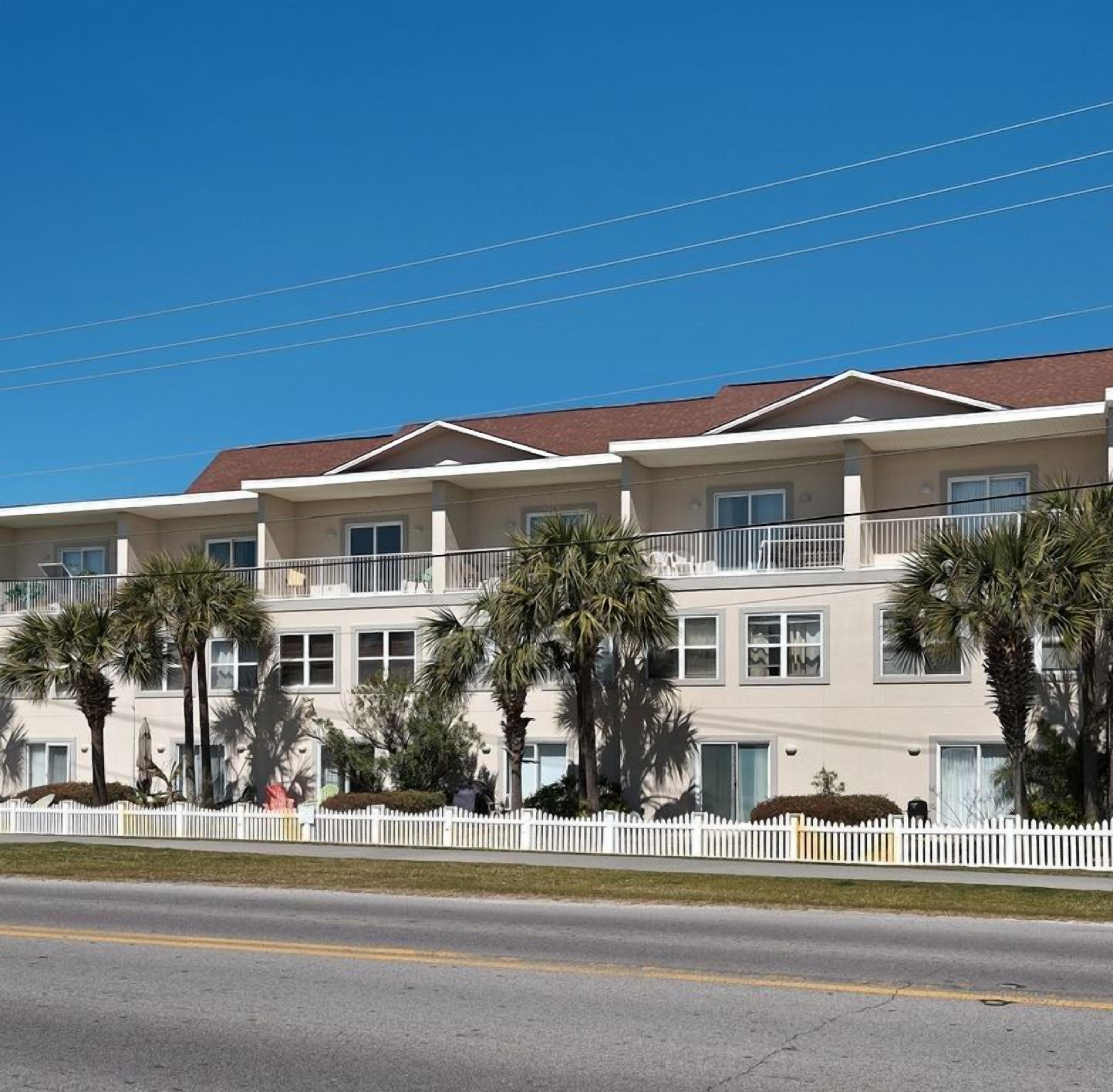 A multi-story hotel with a white facade, balconies, and palm trees.
