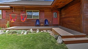 Eine Holzhütte mit Veranda, zwei blauen Stühlen, einer roten Tür und einer Hängematte.