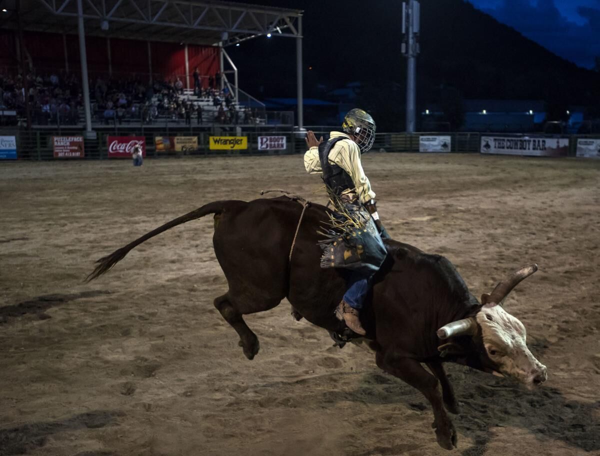 A rodeo event with a rider on a bull in mid-air, surrounded by a dirt arena and a crowd in the background.