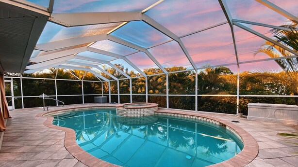 A covered swimming pool with a curved design, surrounded by a patio area with stone tiles. - Modern 3 bedroom, 2 bath getaway with HEATED private pool and jacuzzi (Fort Myers)