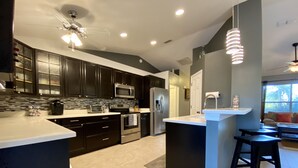 A modern kitchen with dark cabinetry, stainless steel appliances, and a central island with stools. - Modern 3 bedroom, 2 bath getaway with HEATED private pool and jacuzzi (Fort Myers)
