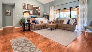 A living room with a sectional sofa, a patterned rug, and a large window with curtains.