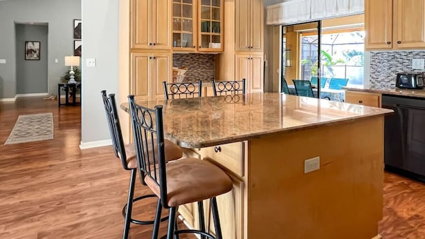 A kitchen with wooden cabinets, a granite countertop, and a dining area with chairs.