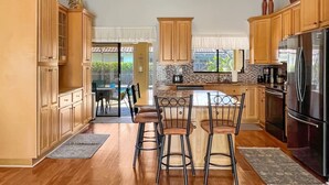 A spacious kitchen with wooden cabinets, a central island with bar stools, a large refrigerator, and a view to the outside.