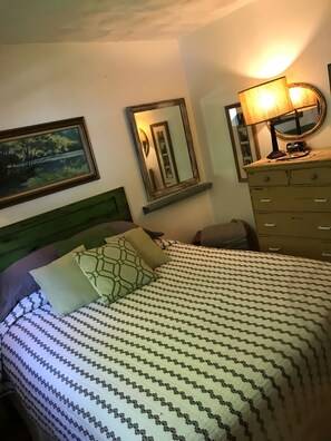 Une chambre à coucher avec un lit, une commode, un miroir et un tableau accroché au mur.