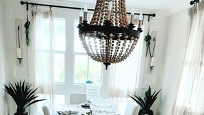 A dining room with a wooden table set for six, white chairs, and a large chandelier.