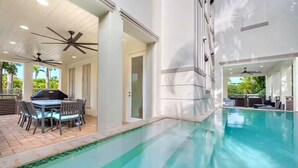 An indoor swimming pool with ceiling fans, a dining area with a table and chairs, and a view of the outdoors.