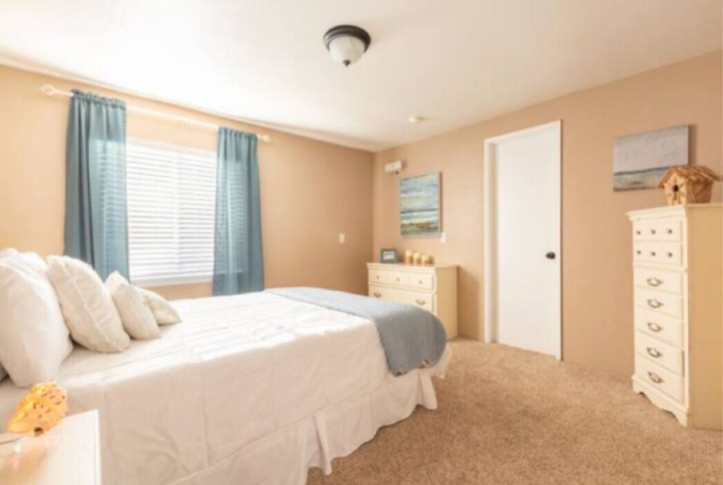 Ein Schlafzimmer mit Bett, Schminktisch, Nachttisch und einem Fenster mit Vorhängen.