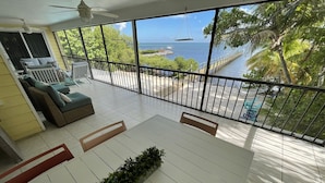 A spacious balcony with a view of the sea, white tiled flooring, and a seating area with cushions and a plant. - Sunset Catch- Gulf Front, Open Water Views, Private Pool and Dock, Kayaks. (Marathon)
