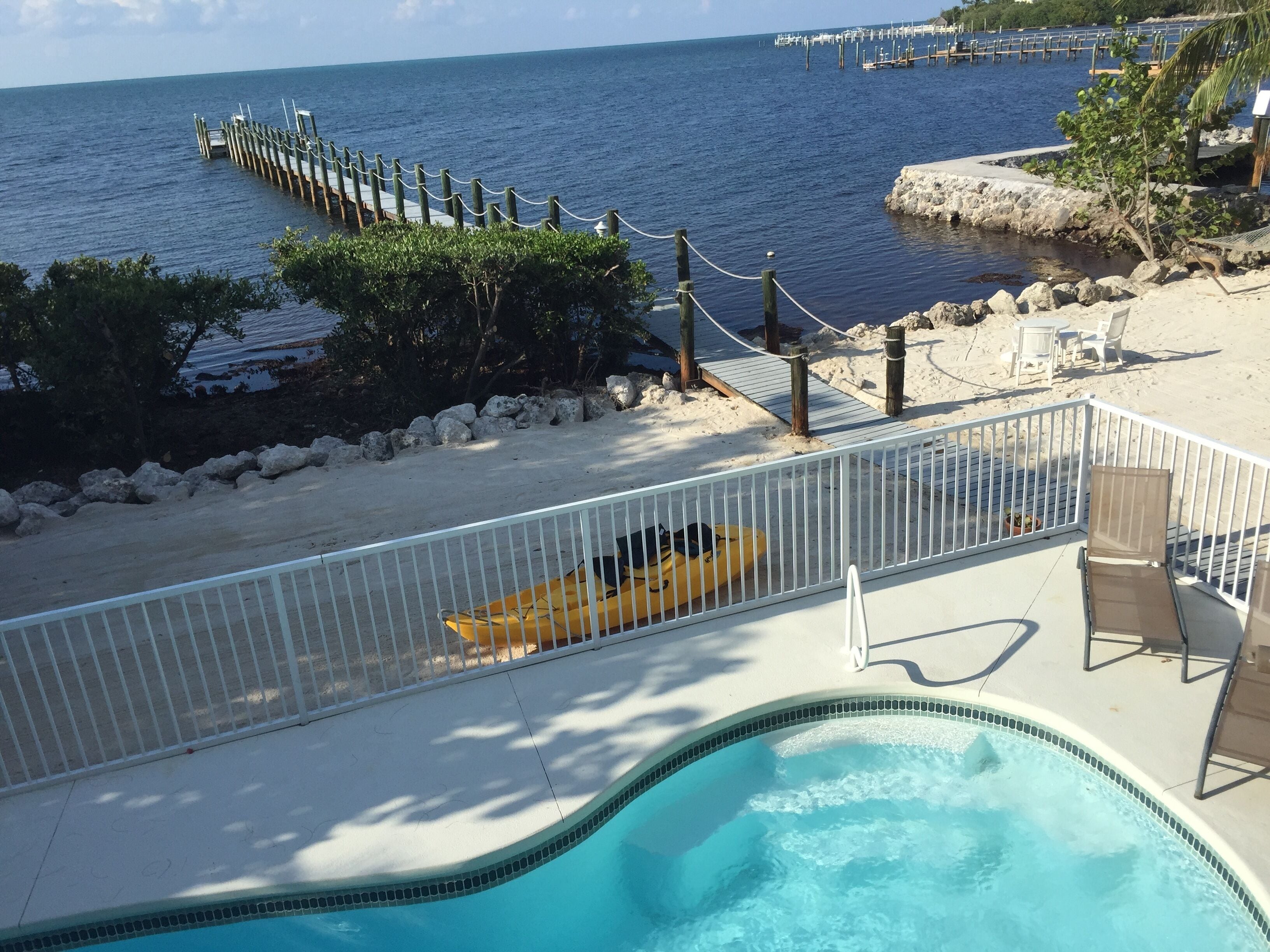 A pool area with a view of the ocean and a dock.