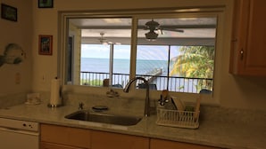 A kitchen with a large window offering a view of the ocean and a dock. - Sunset Catch- Gulf Front, Open Water Views, Private Pool and Dock, Kayaks. (Marathon)