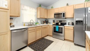 A modern kitchen with wooden cabinets, stainless steel appliances, and a patterned rug. - Fairytale Villa - 2 Masters, Privacy Fence! (Kissimmee)