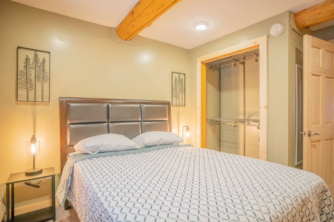 Une chambre à coucher avec un lit, des lampes de chevet, une poutre en bois au plafond et une porte.