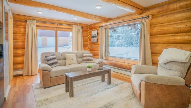 A cozy log cabin interior with a sofa, armchair, and a coffee table. - Tucked Away Timber Lower Suite (Fairbanks)