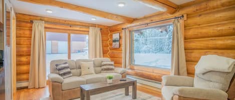 Interior acogedor de una cabaña de troncos con sofá, sillón y una mesa de centro.
