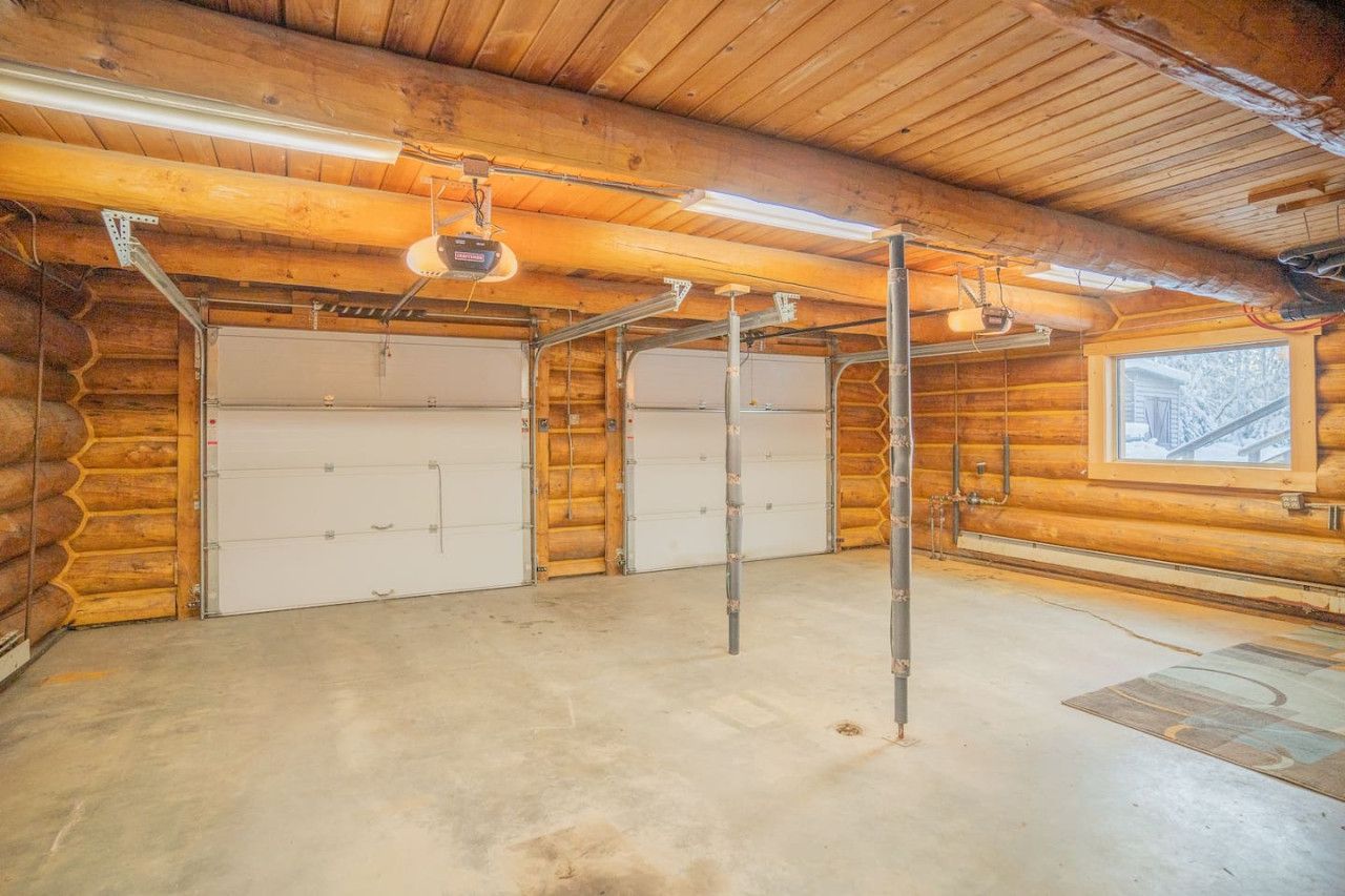 Une cabane en rondins dotée de deux portes de garage, d’un plancher en béton et d’une fenêtre laissant entrer la lumière naturelle.